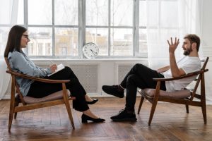 Two people sit in chairs in a room with a clock.