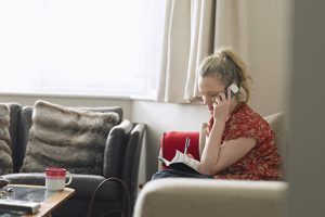 A person sitting comfortably on a couch and chair while explaining something over the phone.