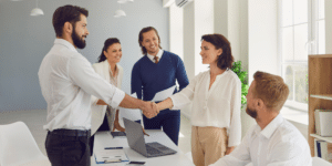A group of professionals in a modern office smiling and shaking hands at the end of a successful HR Outsourcing meeting.