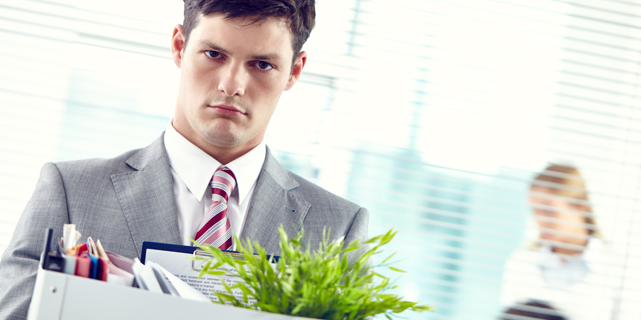 Businessman in a suit holding documents and a plant, leaving an office after termination