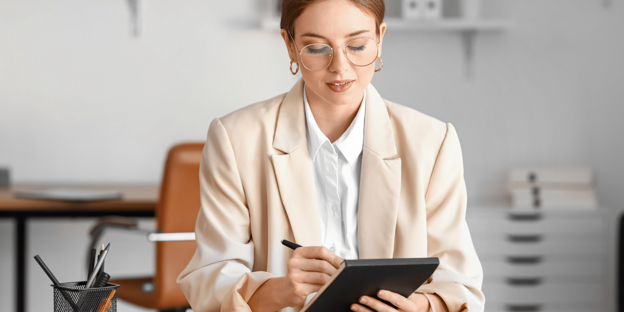 Businesswoman in a modern office writing notes on a tablet during a meeting