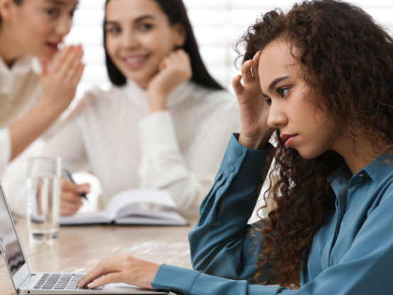 Employee feeling distressed at work while colleagues talk in the background, illustrating workplace bullying or conflict