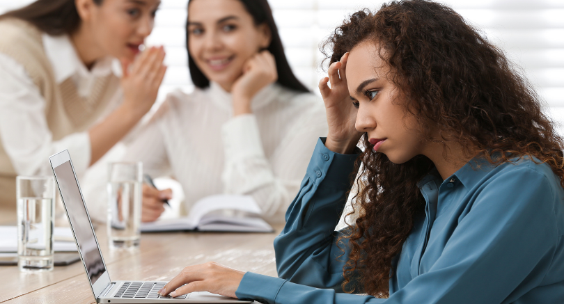 Employee feeling distressed at work while colleagues talk in the background, illustrating workplace bullying or conflict