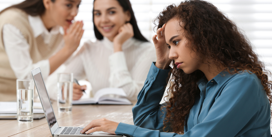 Employee feeling distressed at work while colleagues talk in the background, illustrating workplace bullying or conflict